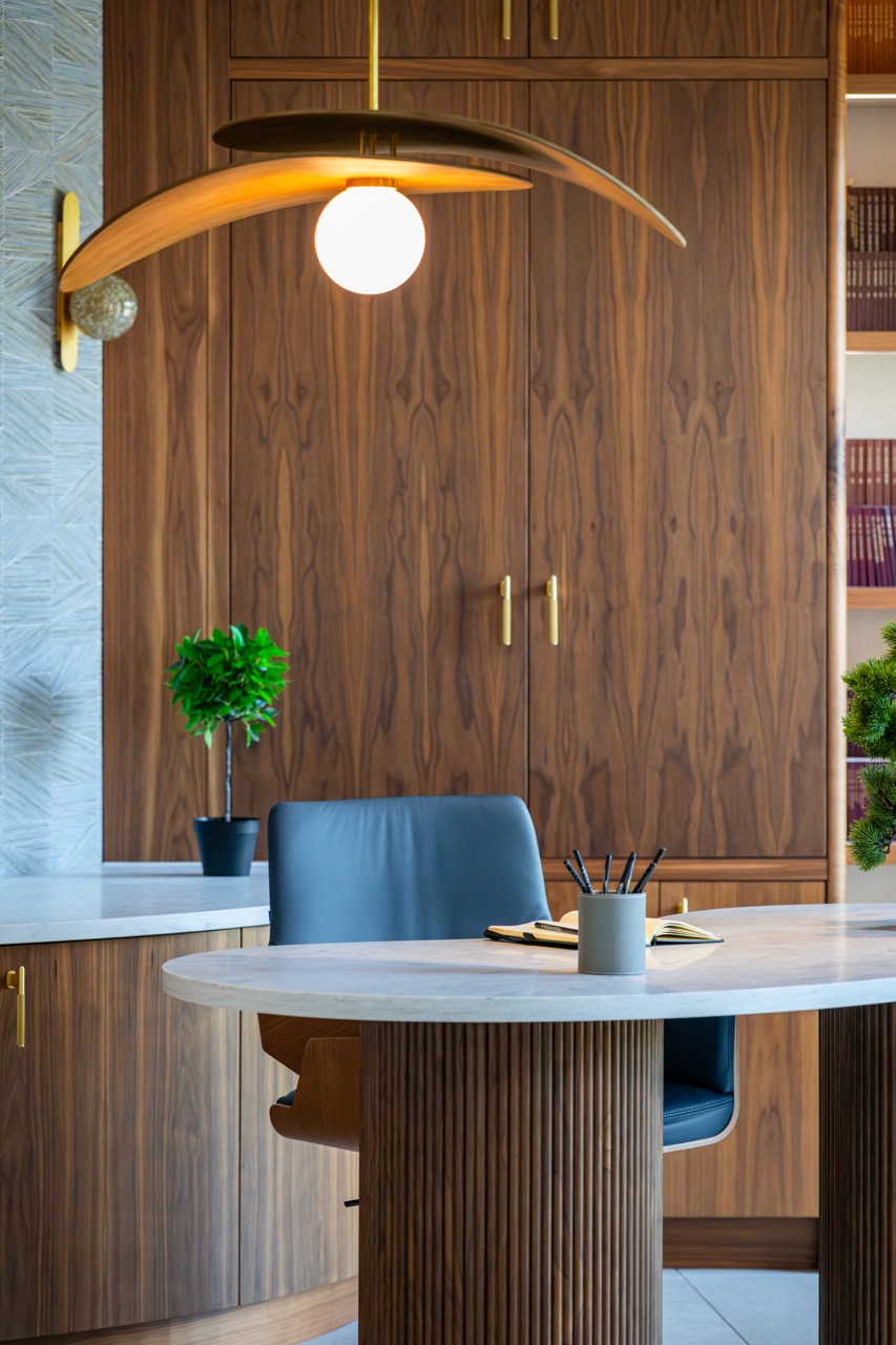 Queens Orchard home office detail — a sculptural wood pendant above a marble-topped fluted desk against bookmatched walnut cabinetry